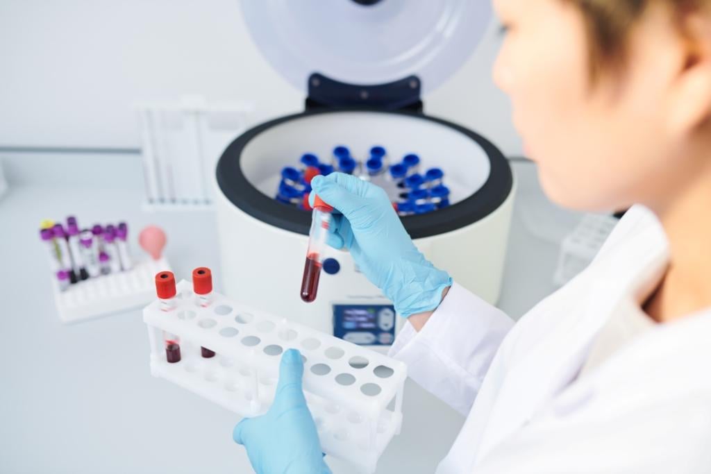 - Microbiologist standing at desk and holding test tube rack while preparing blood samples for centrifuge