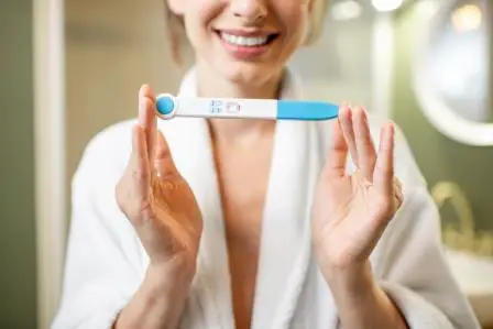 Happy woman holding pregnancy test stick in the bathroom. 
